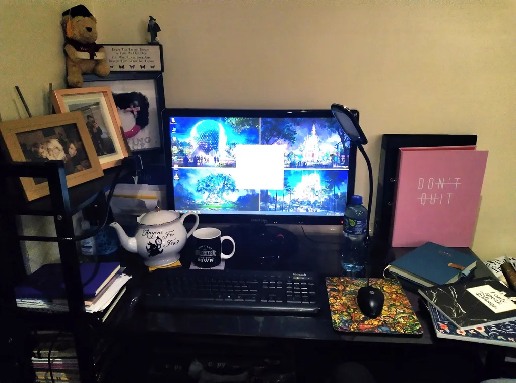 home office setup, Disney screensaver and mousepad, a pot of tea and a mug, photos of family and notebooks dotted around the desk