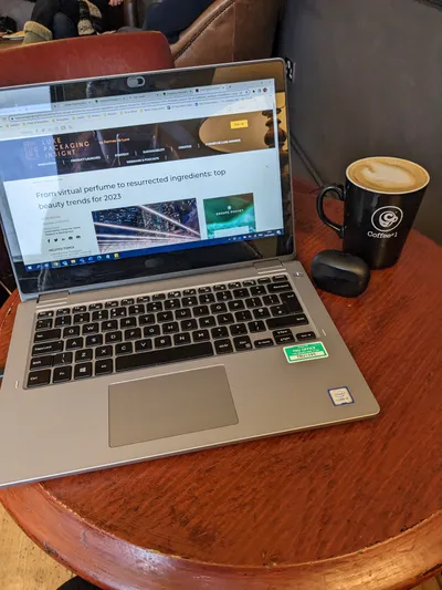 Person typing on a laptop with notebook, pen, phone and mug of tea on the table