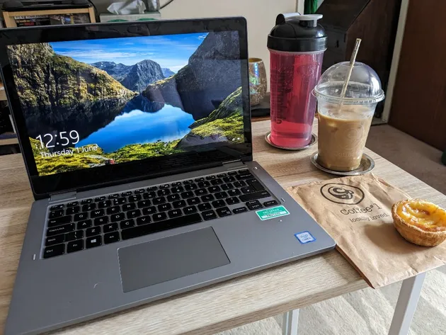 Laptop open on screensaver mode, with a bottle of squash, an iced coffee and a Portuguese tart on the table next to the left.